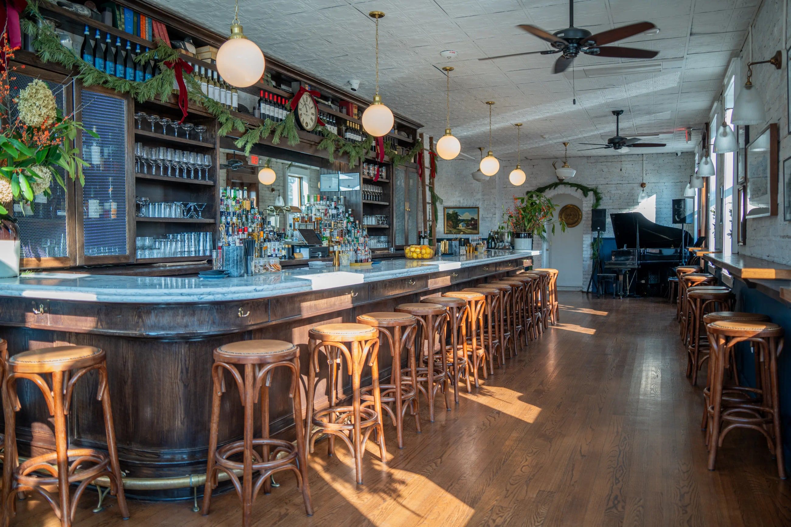 The marble bar at Lyonshare under pendant lights, with wooden stools and a pressed tin ceiling.