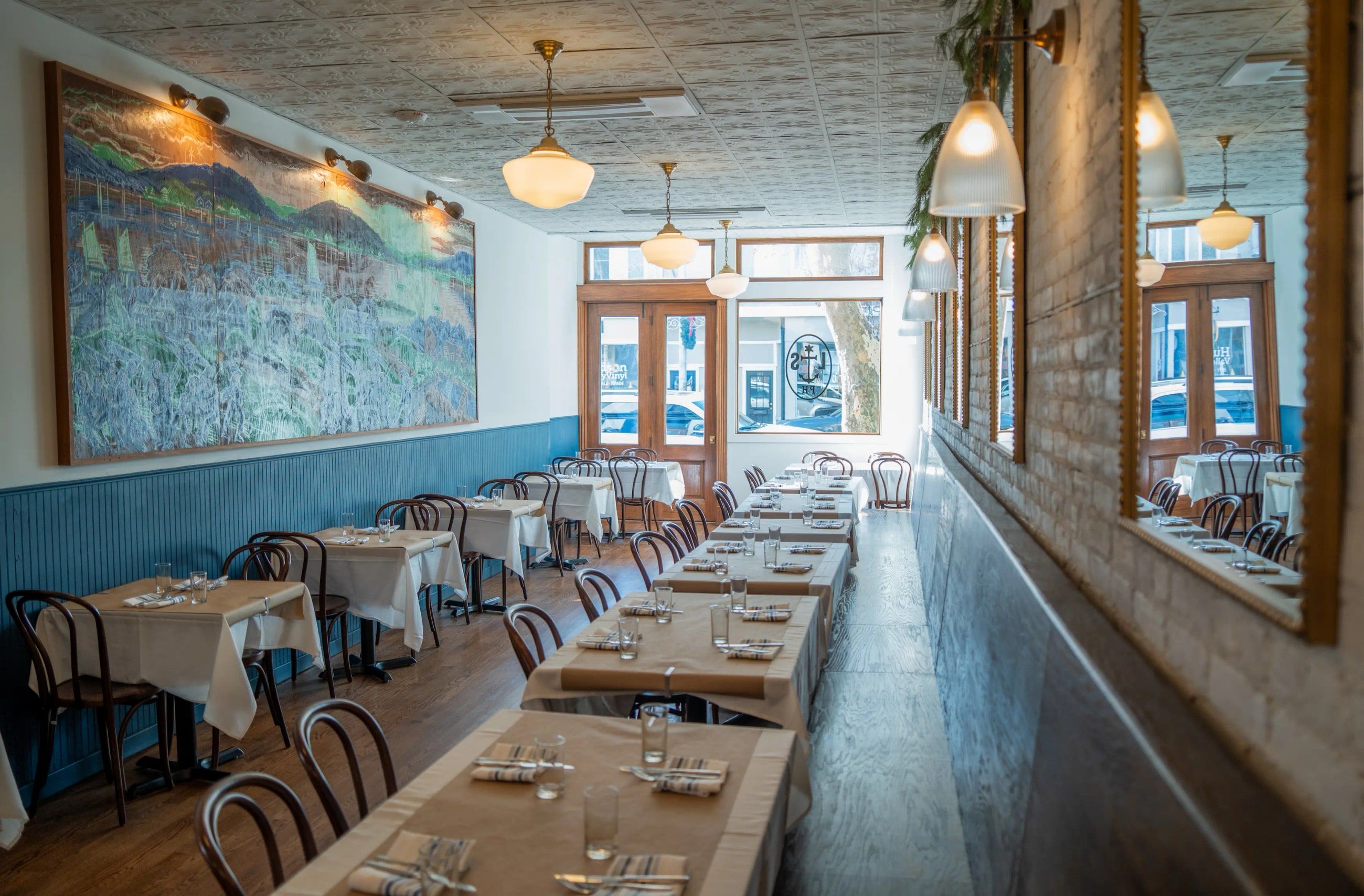 Lyonshare’s dining room set for service, with long banquette tables beneath a Hudson Valley mural.