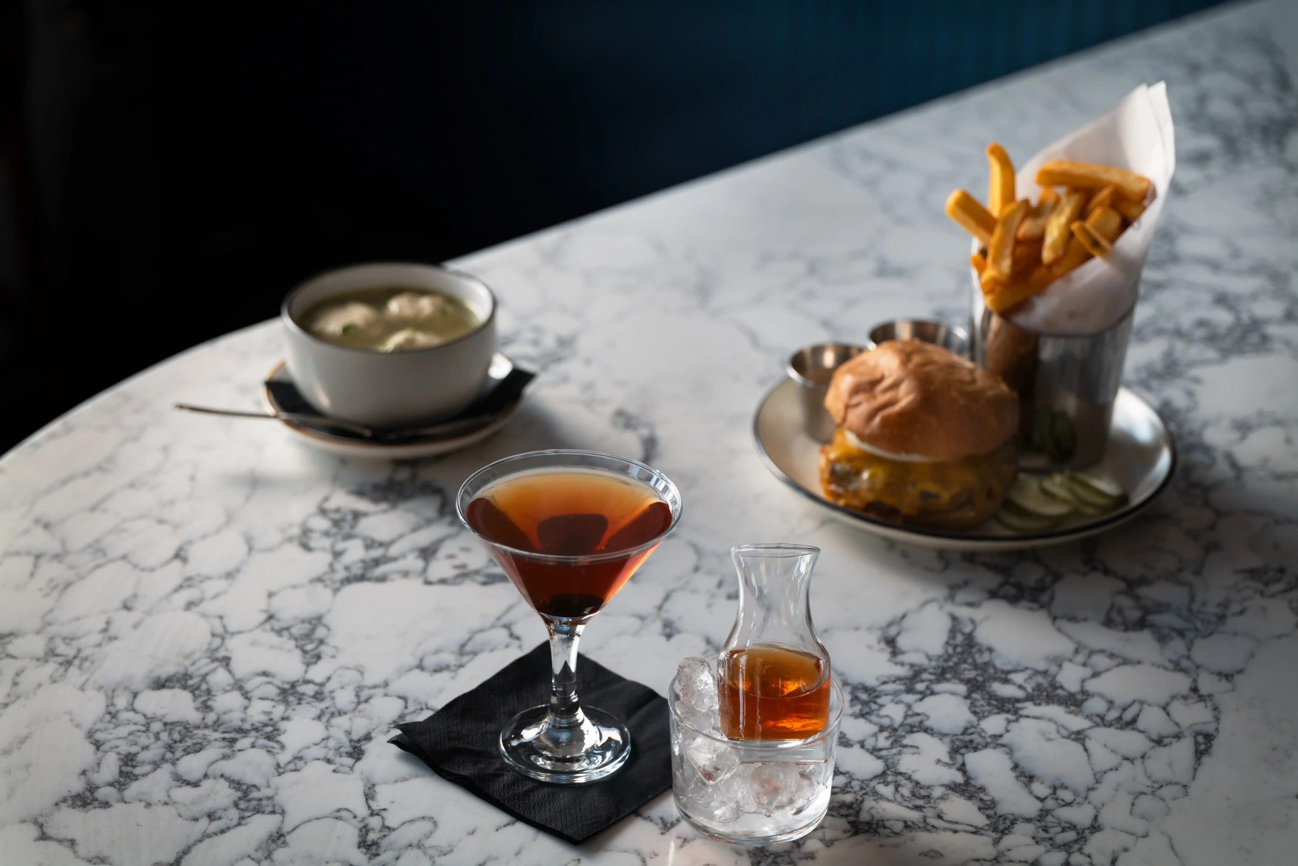 A cocktail, a burger and fries, and a cup of soup on Lyonshare’s marble bar.