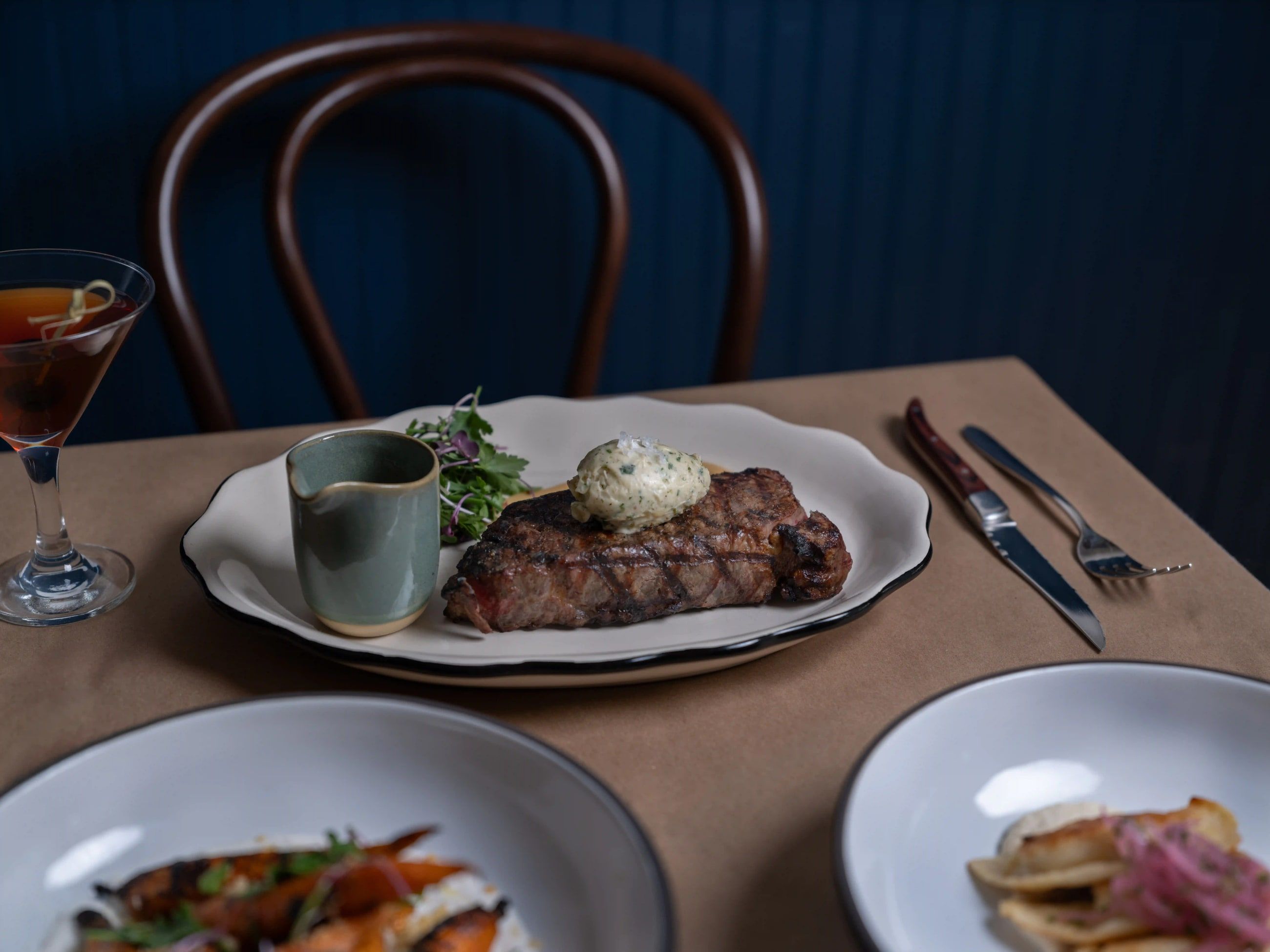 A New York strip with compound butter, a martini and shared plates on a dining table at Lyonshare.
